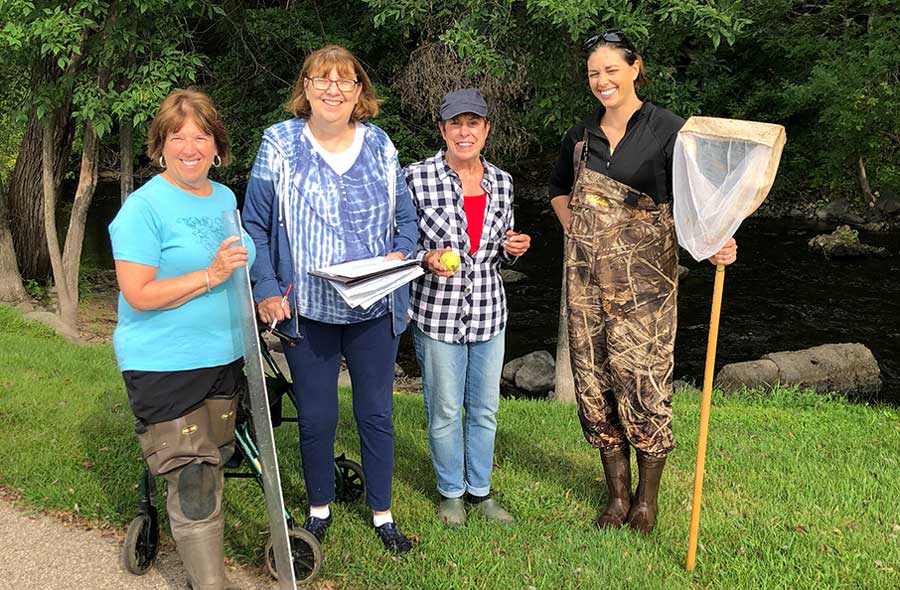 A group of four woman stand in a grassy field. They are each holding a piece of monitoring equipment.