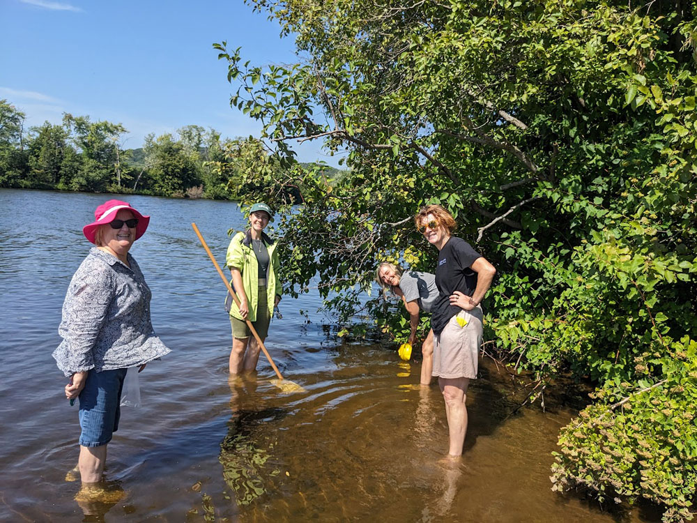 4 people standing in shallow water on a rivers edge