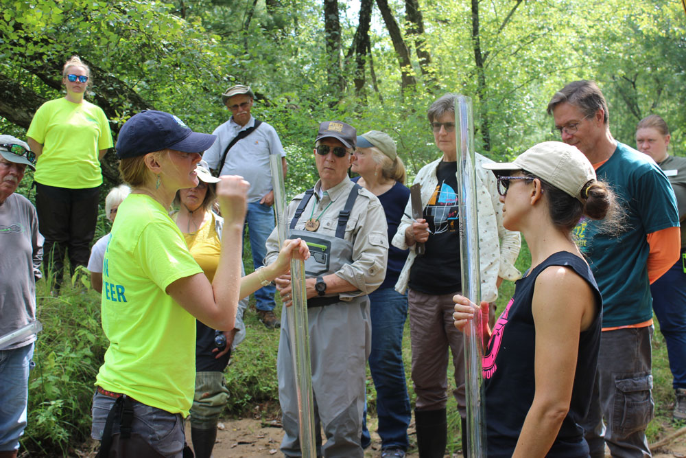 A group of people outside learn about measuring water clarity with transparency tubes.