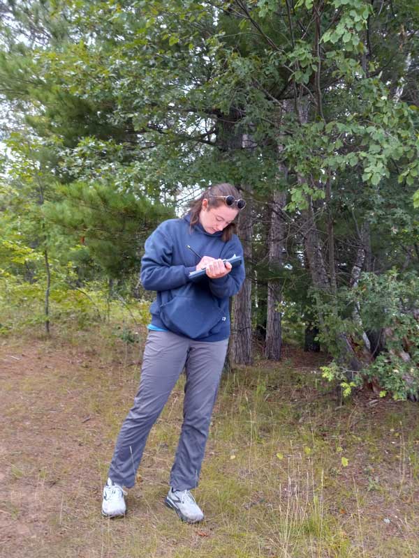 A woman in a wooded area writing on a clipboard