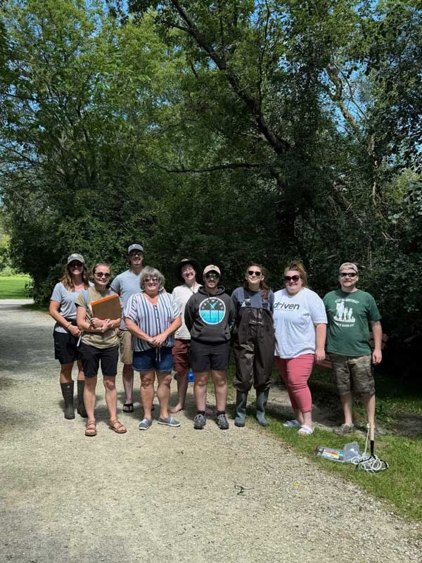A group of people standing in front of a wooded area
