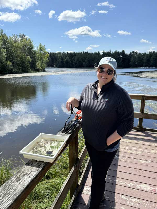 A woman standing on the end of a pier with a lake in the background