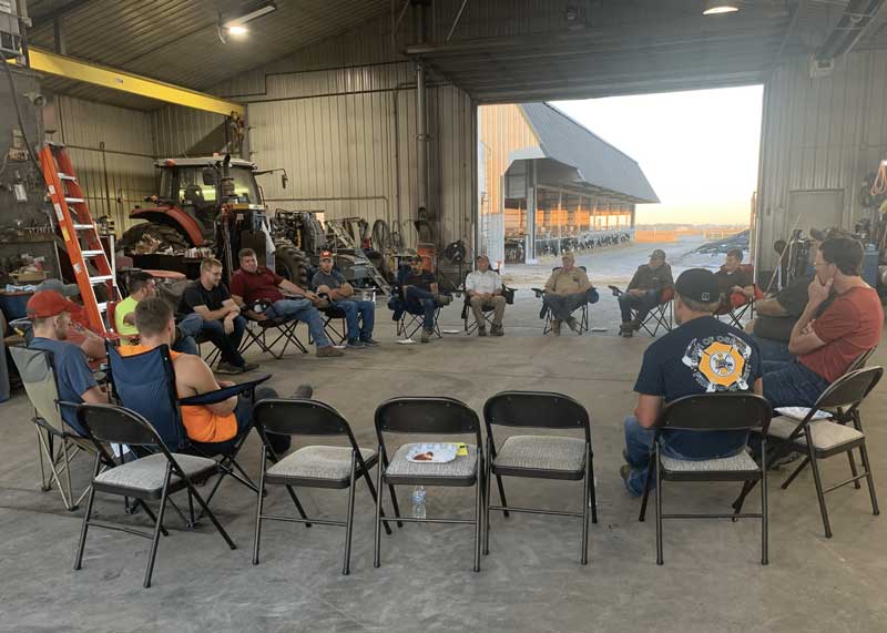 A group of people sitting on chairs setup in a large circle inside a metal barn
