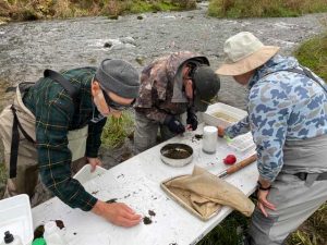 Three people looking at samples collected from the river in the background