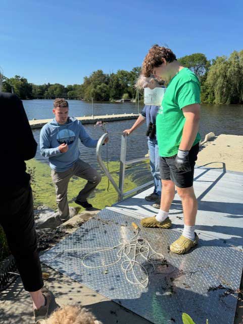 A small group of people gathering samples from a pier in a lake