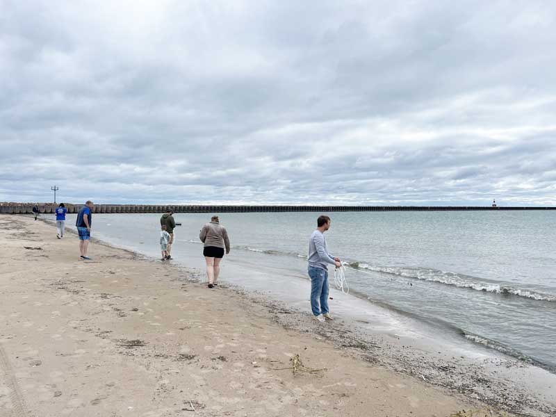A group of people on a sandy beach casting rake drags into the water