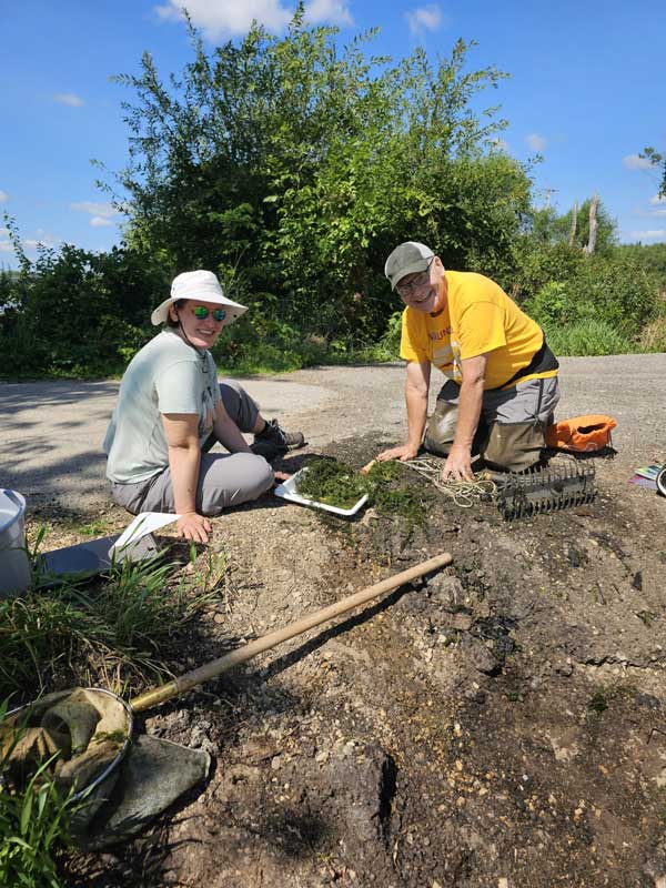 Two people on a steep shoreline gathering samples