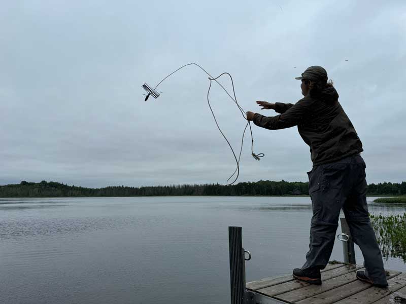 A man casting out a rake into a lake from the end of a pier