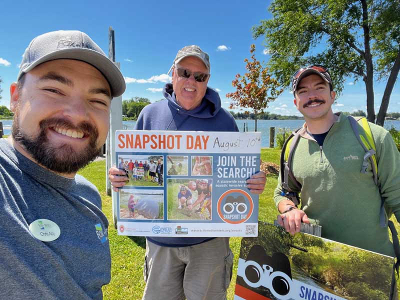 Three volunteers holding up a snapshot day sign