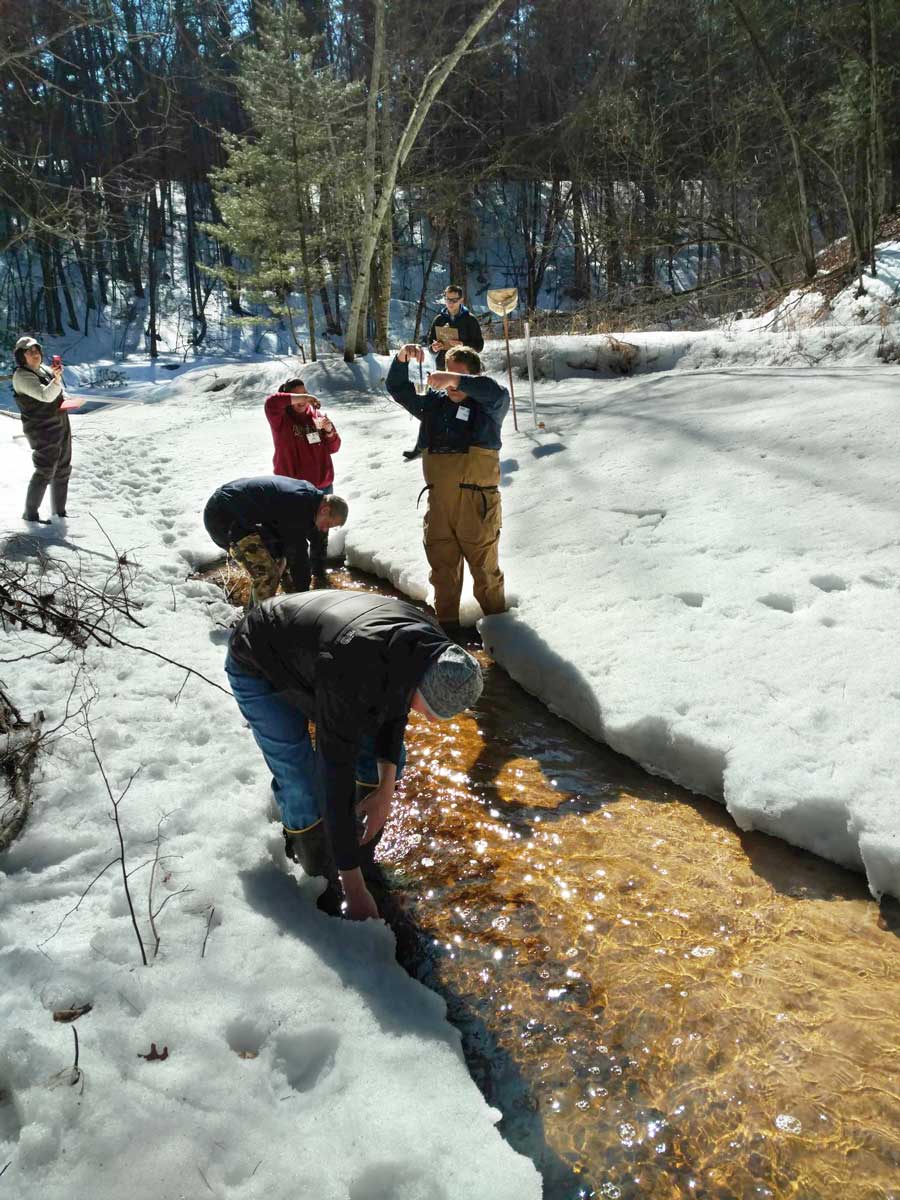 A group of volunteers testing a small creek running through a snow covered opening in the winter