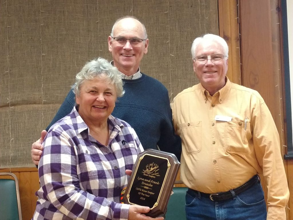 Frank and Lynn smile at the camera holding an award plaque, with another person standing next them.