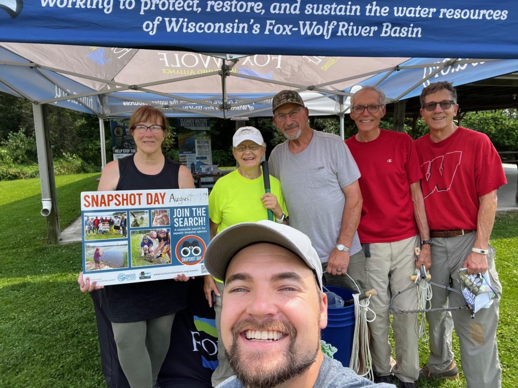 Five volunteers pose for a photo. Four stand under an awning. One person stands in front of them. 