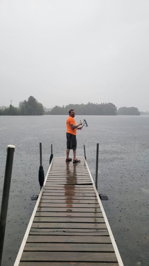 A man wearing an orange shirt and shorts stands at the end of a dock. It is a hazy day. 