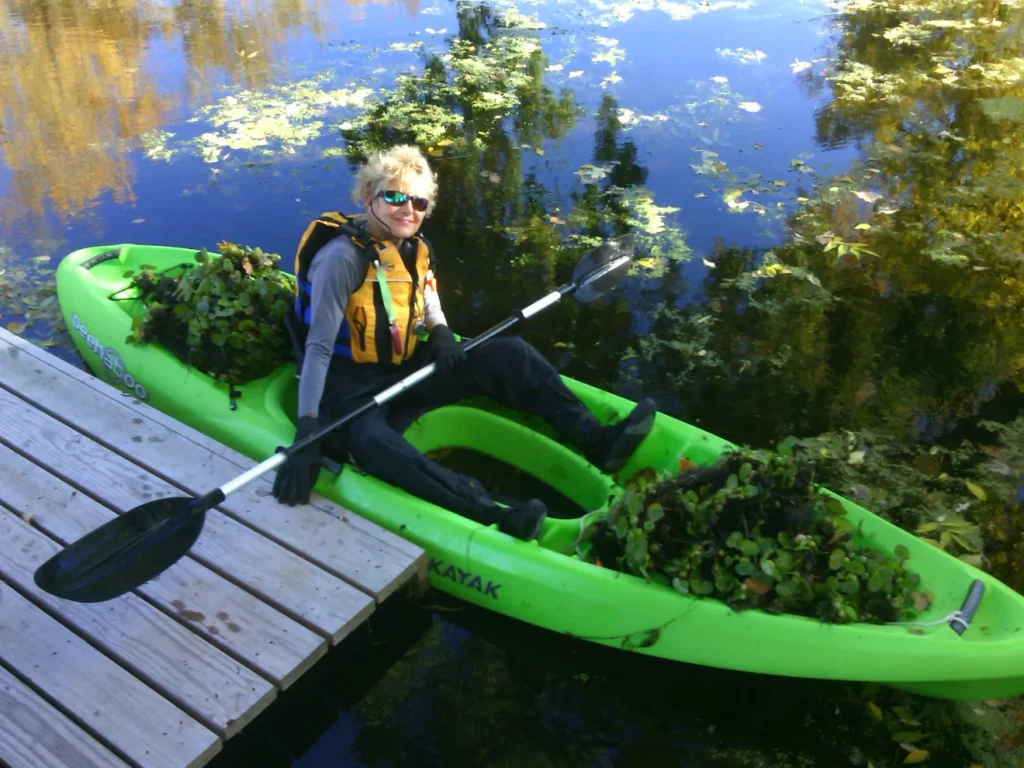 A woman sitting in a bright green kayak along side a pier