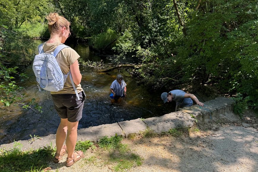 A girl with a backpack watching two other people in a stream