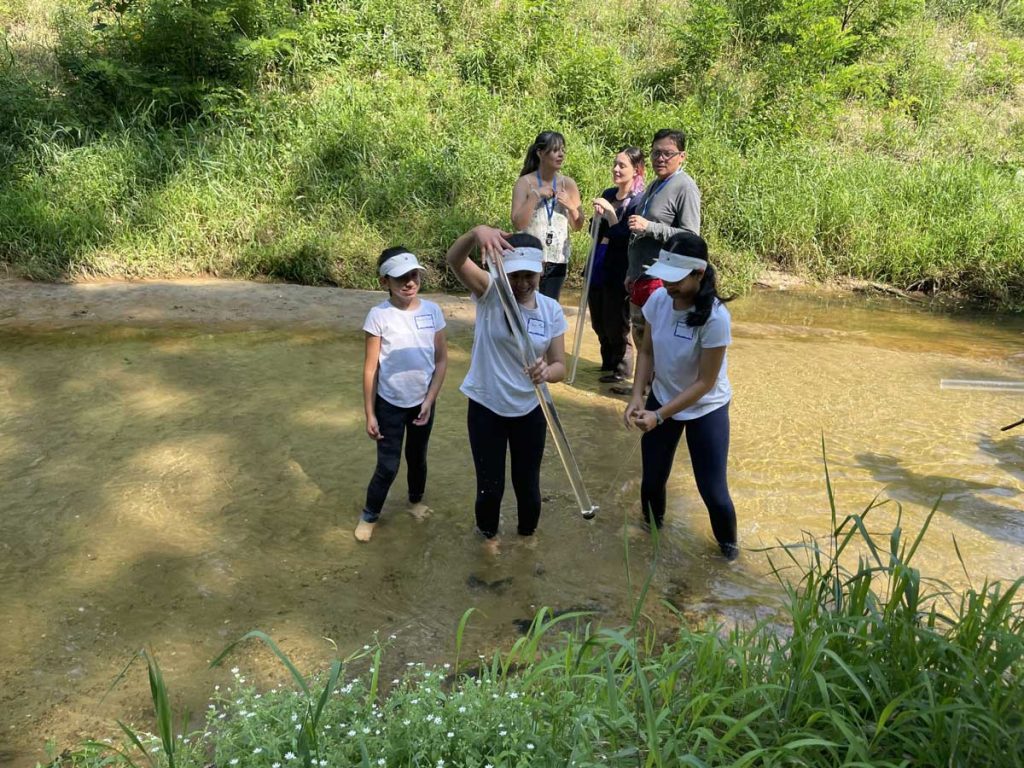 A group of youth and adults taking water clarity measurements in a stream with transparency tubes.