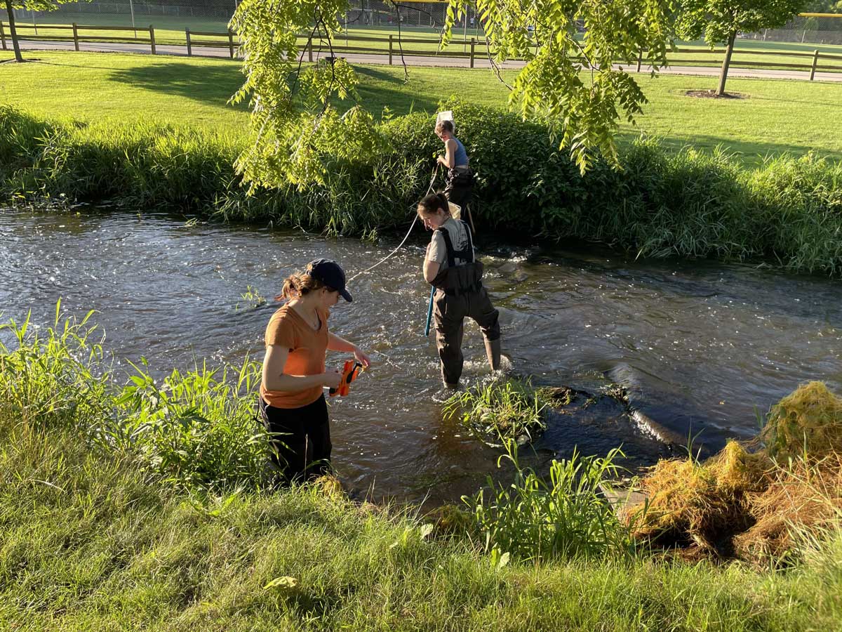 Three volunteers measure the width of stream during a sunny afternoon