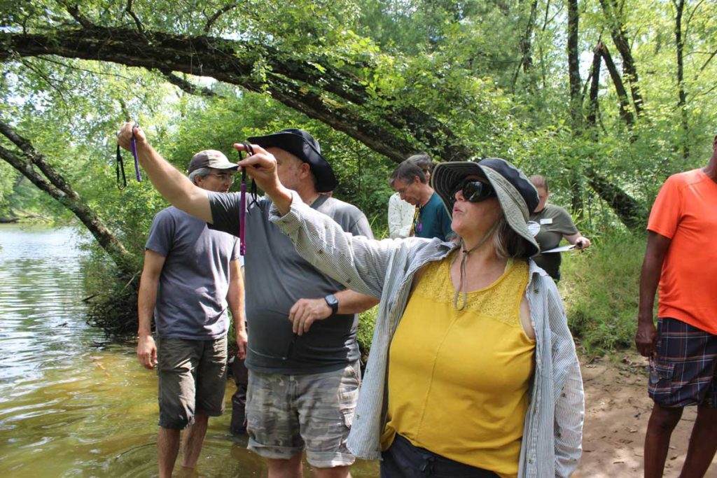 A group of people stand in a river and look at thermometer readings.