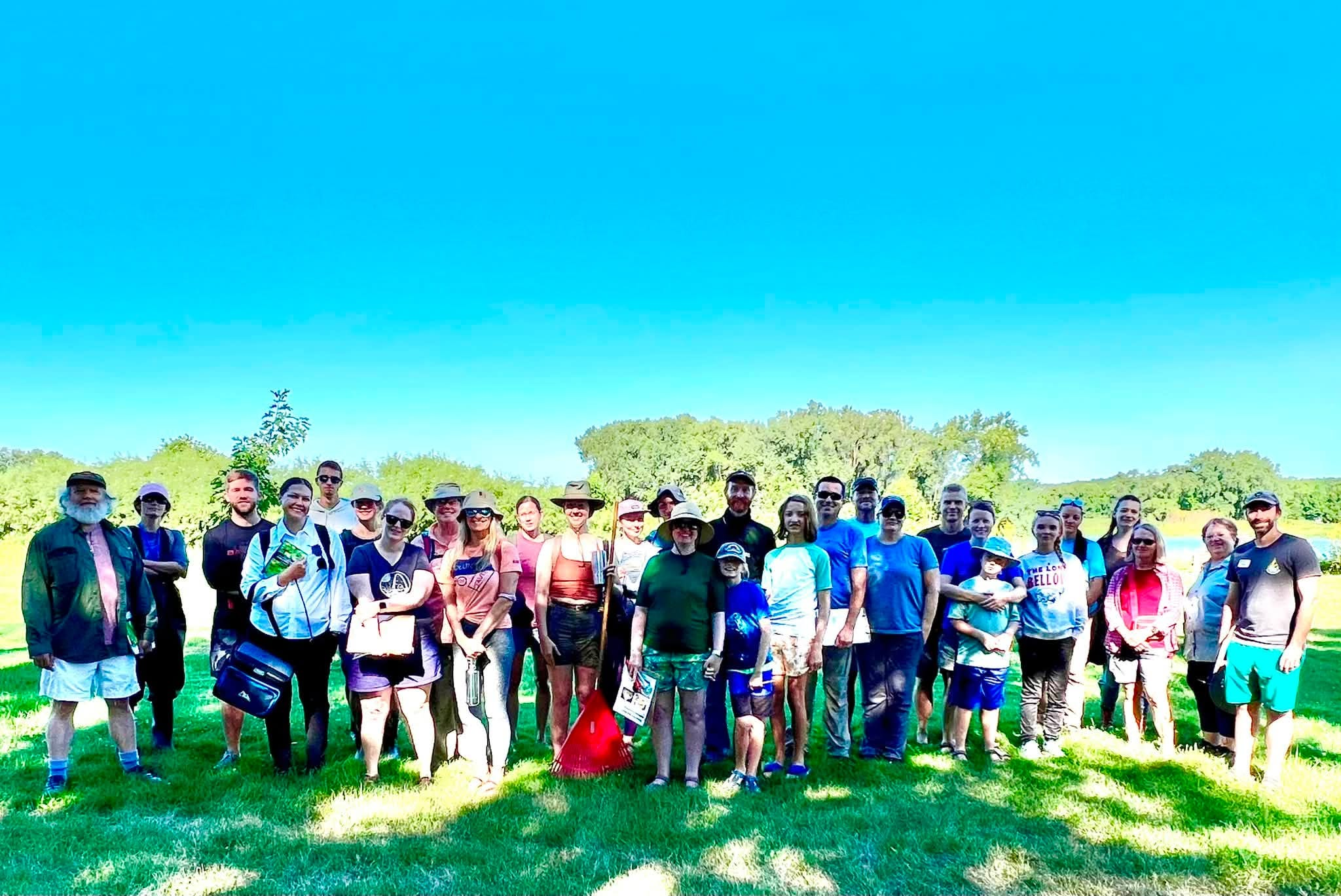 A large group of people stand in the shade on a sunny day.